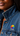 Close-up of a person wearing a blue denim jacket, featuring a colorful circular pin with rainbow segments and the text '#CRAZY' on the chest.