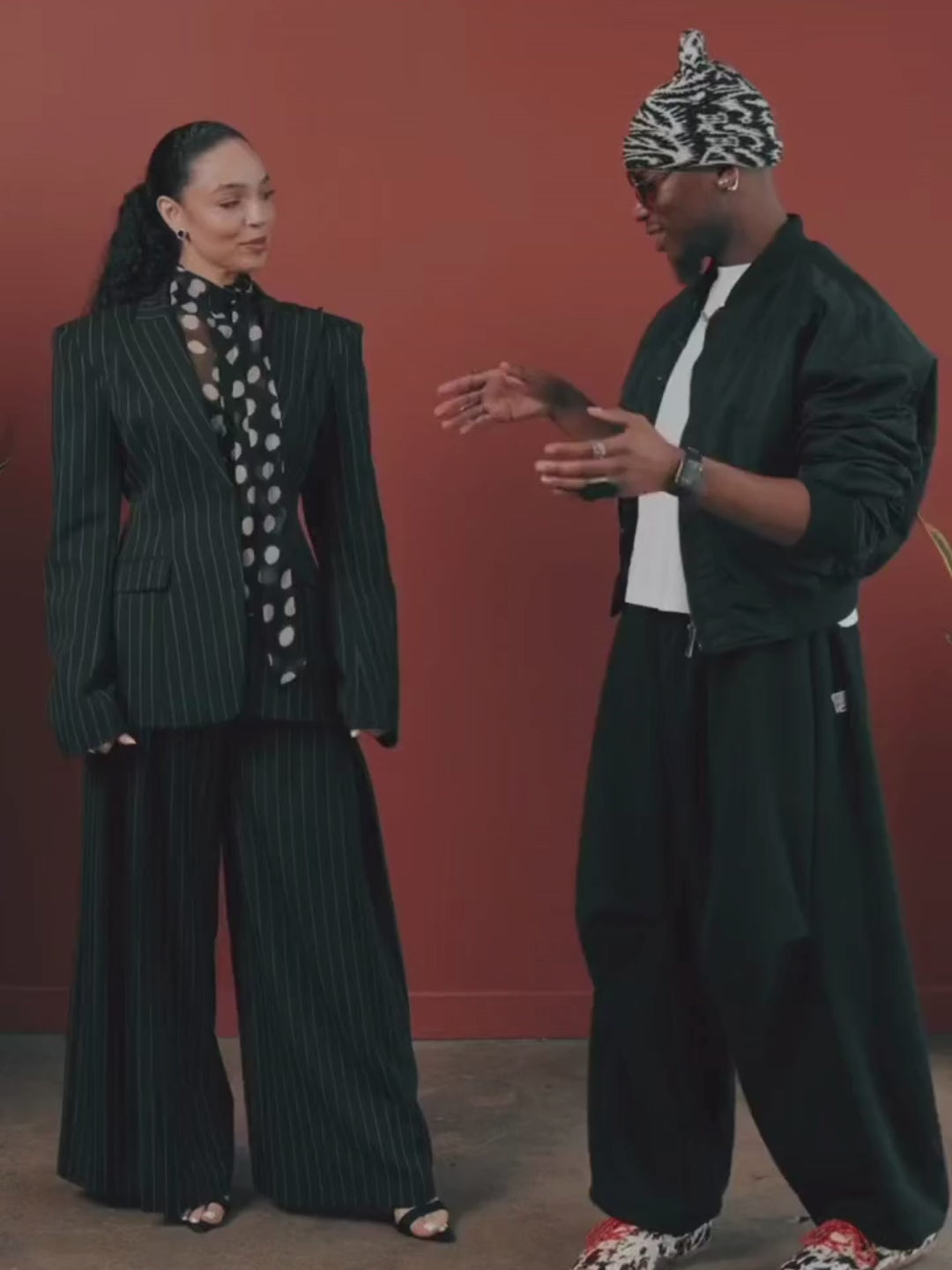 Person styling a woman in a pinstripe suit with a polka dot top. Red background with cement flooring.